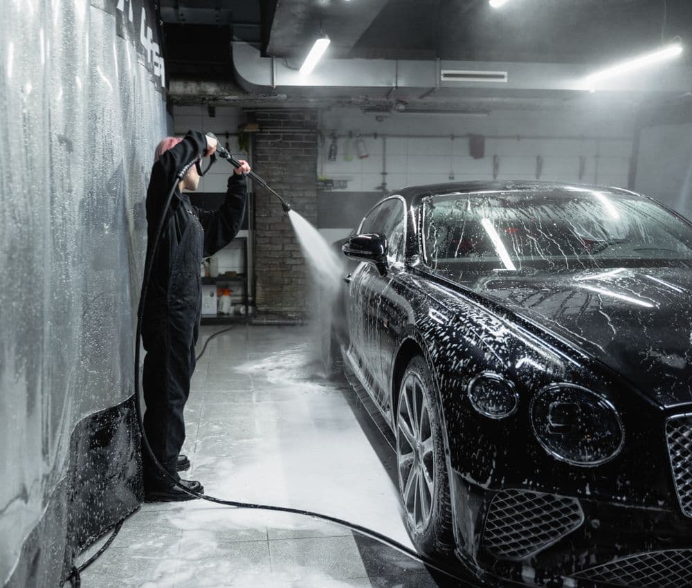 Professional pressure washing a soapy black car